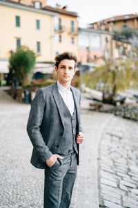 Portrait of young man standing on street against buildings