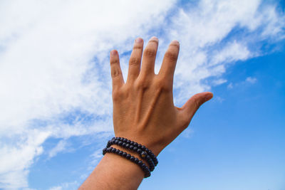 Cropped hand of man reaching blue sky