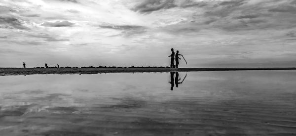 Silhouette people standing by sea against sky