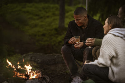 Friends sitting by campfire and drinking wine