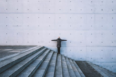 Front view of woman standing with arms outstretched on steps against gray wall