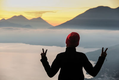 Woman standing on mountain in foggy weather against sky during sunset