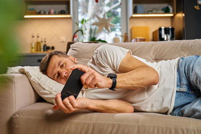 Young woman using phone while sitting on sofa at home