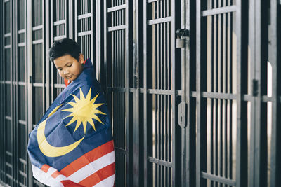 Side view of boy wearing malaysian flag by fence