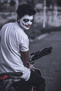 Portrait of man with face paint sitting on motorcycle at road