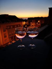 Wine glass on table in city against sky during sunset