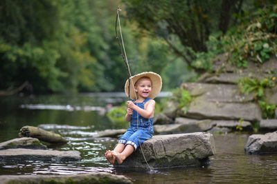 Funny happy little kid fishing at the lake. a fisher boy sits in the lake with a fishing rod