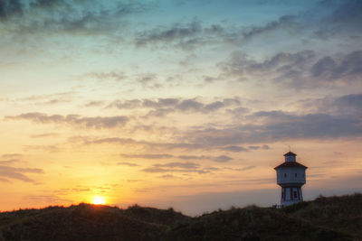 Lighthouse by sea against sky during sunset