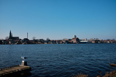 Buildings by canal against clear blue sky