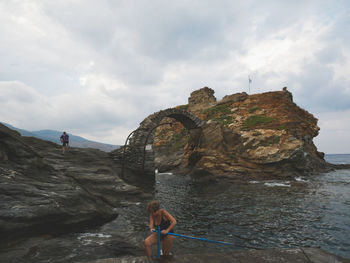 Man standing on rock by sea against sky