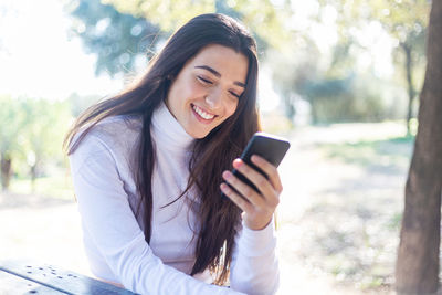 Smiling young woman using mobile phone while sitting in park