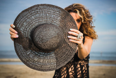 Midsection of woman holding hat at beach against sky