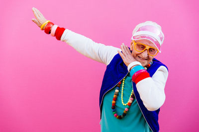 Smiling senior woman gesturing against pink background