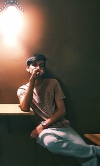 Young woman looking away while sitting on table against wall