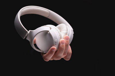 Close-up of hand holding headphones against black background