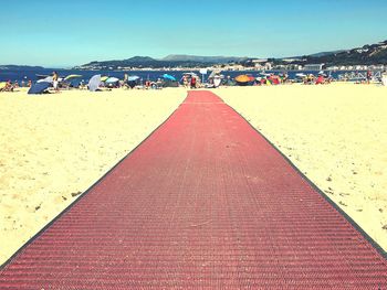 Tilt image of people on beach against clear blue sky