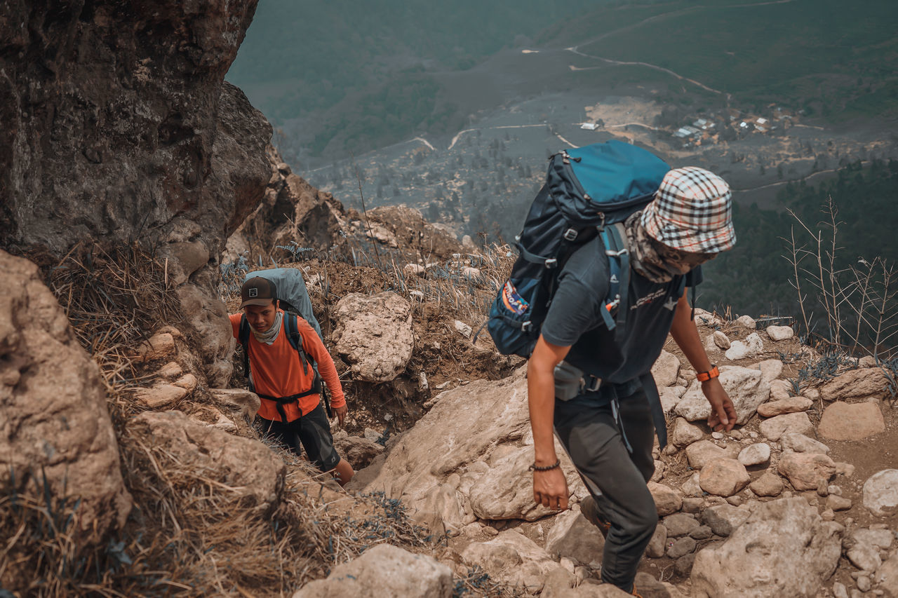 REAR VIEW OF PEOPLE WALKING ON ROCKS