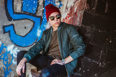 Portrait of young woman sitting against graffiti wall