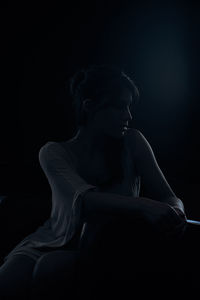 Woman looking away while sitting against black background