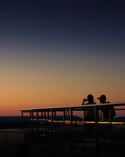 Silhouette people on footbridge against sky during sunset