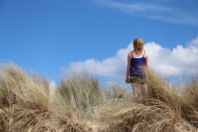 Rear view of woman standing amidst grass against sky