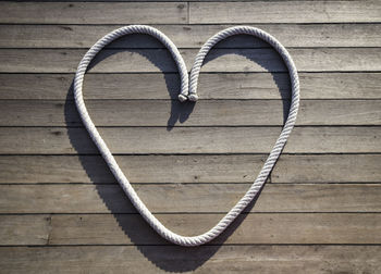 High angle view of rope arranged in heart shape over wooden plank