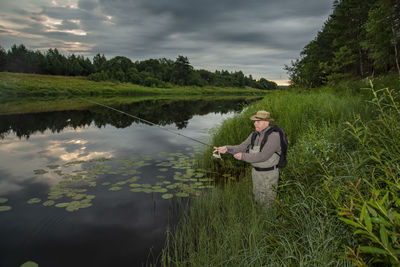 Mature man fishing at lake against sky