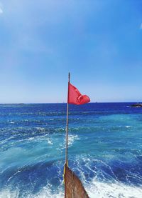 Red flag on sea against clear blue sky