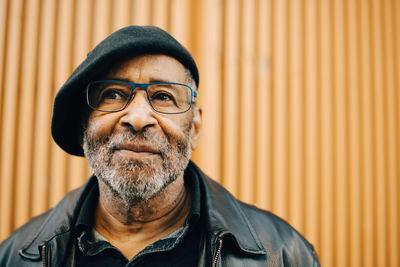 Smiling senior man with eyeglasses against wall