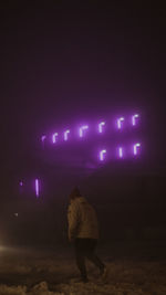 Rear view of people walking on illuminated street lights at night