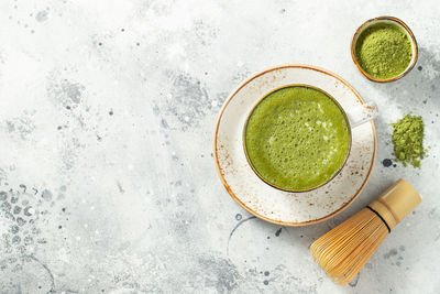 Matcha green tea latte in a cup with cream on a light concrete background. 