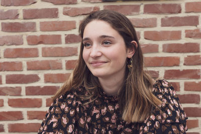 Close up shot of a beautiful brown haired teenager smiling, against a red brick background