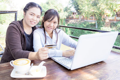 Smiling young woman using phone while sitting on table