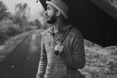 Mid adult man holding umbrella while standing against road