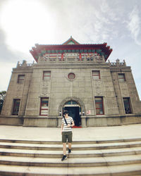 Low angle view of woman standing by building against sky