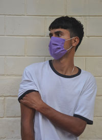 Young man wearing mask standing against wall