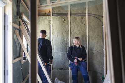 Female electrician with drill machine talking with male coworker