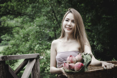 Smiling woman holding basket while standing outdoors