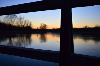 Close-up of silhouette railing by lake against sky during sunset