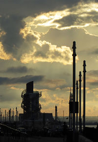 Silhouette factory against sky during sunset