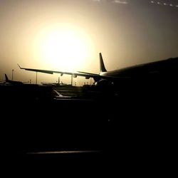 Silhouette airplane on runway against sky during sunset