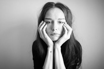 Portrait of mid adult woman with hands on chin standing against wall