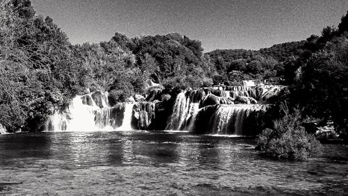 Scenic view of waterfall in forest against sky