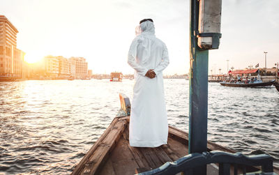 Rear view of man standing in boat on river at sunset