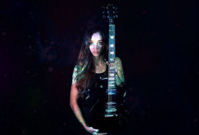 Portrait of woman holding guitar in darkroom