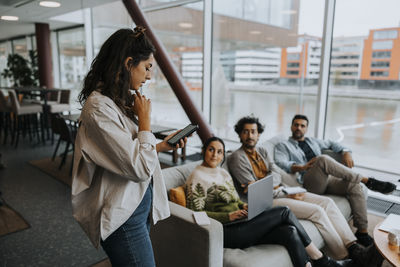 Young businesswoman holding smart phone while discussing strategy with colleagues in office