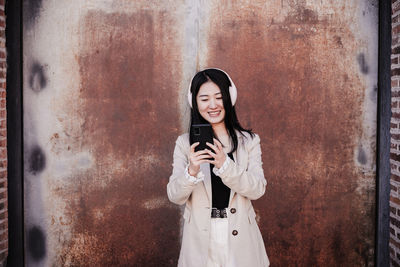 Happy business woman listening to music on headphones and mobile phone in city