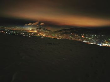 Illuminated city by sea against sky at night