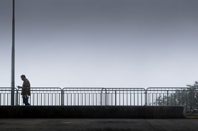 Man standing on railing by bridge against clear sky