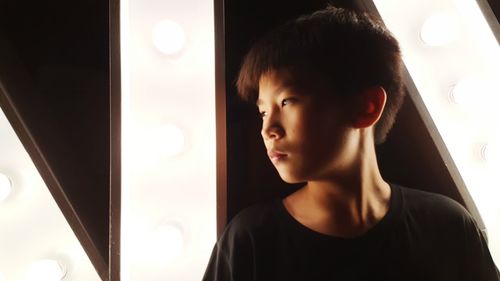 Close-up of boy looking away while standing against illuminated wall